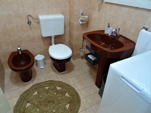 Ein Badezimmer mit Toilette, Bidet, Waschbecken und einem kleinen Teppich.
