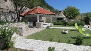 A stone patio with outdoor seating, a small garden, and a stone building with a red-tiled roof. - Holiday Home Stari Zoganj - Two Bedroom Holiday Home With Terrace and Swimming Pool (Orebic)