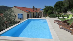 A rectangular swimming pool with a tiled edge, surrounded by a patio with lounge chairs and a small garden area. - Holiday Home Stari Zoganj - Two Bedroom Holiday Home With Terrace and Swimming Pool (Orebic)