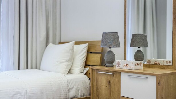 A neatly made bed with white linens, a wooden nightstand with two lamps and a box of tissues. - Escan Tower- Dubai Marina (Dubai)