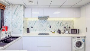 A modern kitchen with white cabinetry, a built-in microwave, a coffee maker, and a washing machine. - Escan Tower- Dubai Marina (Dubai)