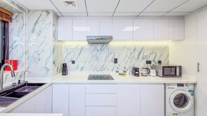 A modern kitchen with white cabinetry, a built-in microwave, a coffee maker, and a washing machine. - Escan Tower- Dubai Marina (Dubai)
