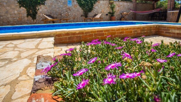 A pool area with stone walls, a wooden pergola, and a flower bed with purple flowers. - Apartments Andre Porec - Two Bedroom Apartment With Balcony and Pool (Porec)