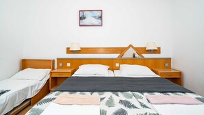 Hotellihuone, jossa on puinen sängynpääty, kaksi yöpöytää, harmaan ja valkoisen kuvioinnin omaava sängynpeite ja yksi seinälle kiinnitetty lamppu.