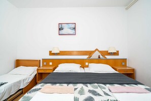 Ein Hotelzimmer mit hölzernem Kopfteil, zwei Nachttischen, einem Bett mit grau-weiß gestreifter Bettdecke und einem Gemälde an der Wand.
