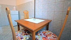 Un pequeño comedor con una mesa y sillas de madera, un papel blanco sobre la mesa y un refrigerador al fondo.