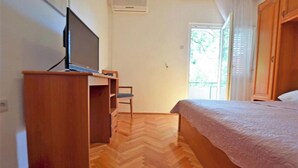 Un dormitorio con una cama, un escritorio de madera con televisor, una silla y un ventanal con cortinas.