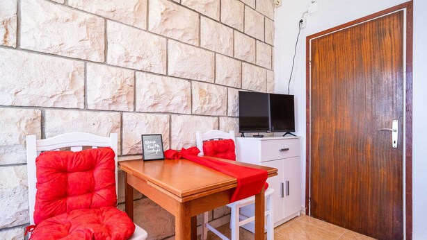 A small room with a stone wall, a wooden door, a TV on a cabinet, and two red cushioned chairs. - Apartments Nikolina - Studio With Sea View (Lumbarda)
