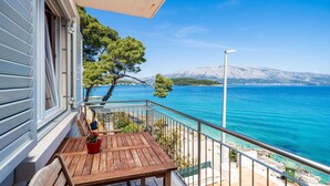 A balcony with a wooden table and chairs, overlooking a clear blue sea and a snow-capped mountain in the distance. - Apartments Nikolina - Studio With Sea View (Lumbarda)