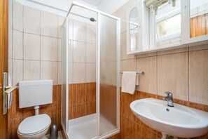 Ein modernes Badezimmer mit Duschkabine aus Glas, Toilette, Waschbecken und Spiegel über dem Waschbecken.