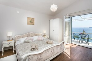 Ein Schlafzimmer mit einem Bett, Nachttischen, einem Kleiderschrank und Meerblick durch eine Schiebetür.