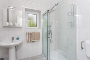 Ein modernes Badezimmer mit einer gläsernen Dusche, einem Waschbecken und einem Fenster über dem Spiegel.