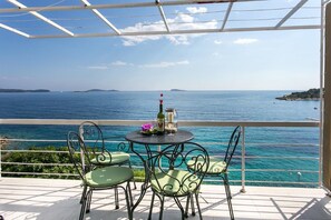 Eine Terrasse mit Tisch und Stühlen mit Blick auf das klare, blaue Meer und entfernte Inseln.