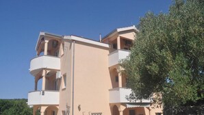 Un edificio de varios pisos con balcones, un muro de piedra y un árbol.