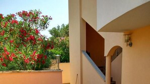 Un patio al aire libre con una mesa, sillas, una escalera y un jardín con flores rojas.