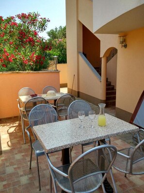 Eine Terrasse im Freien mit Tisch und Stühlen, eine Treppe und ein Garten mit roten Blüten.