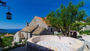 A stone building with a tiled roof, a circular stone structure, and a view of the sea. - Apartment With sea View in Orasac (Dubrovnik)