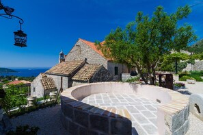 A stone building with a tiled roof, a circular stone structure, and a view of the sea. - Apartment With sea View in Orasac (Dubrovnik)
