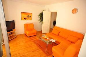 Ein Wohnzimmer mit einer Couch, einem Sessel, einem Couchtisch, einem Fernseher und einem Gemälde an der Wand.