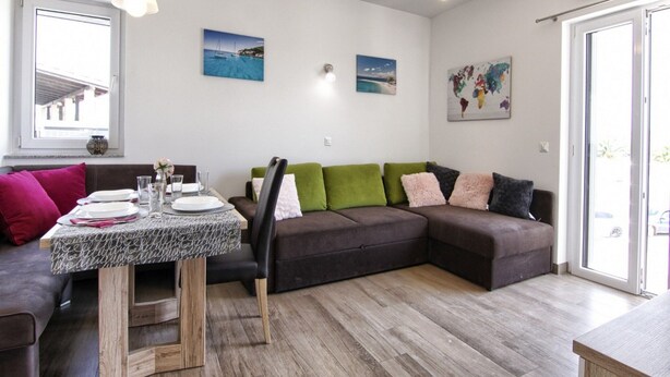 A modern living room with a dining area, featuring a wooden table, a sofa with cushions, and a world map on the wall. - Apartments Victoria - One Bedroom Apartment With Terrace and Sea View (Pakostane)