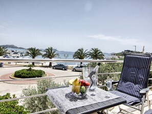 Ein Balkon mit Tisch, Stuhl und Blick auf einen Hafen und das Meer.