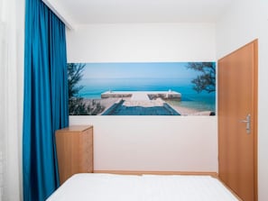 A bedroom with a bed, a wooden dresser, a door, and a wall with a scenic view of a beach and pier. - Apartments Antonio - One Bedroom Apartment With Balcony - 1 (Tucepi)