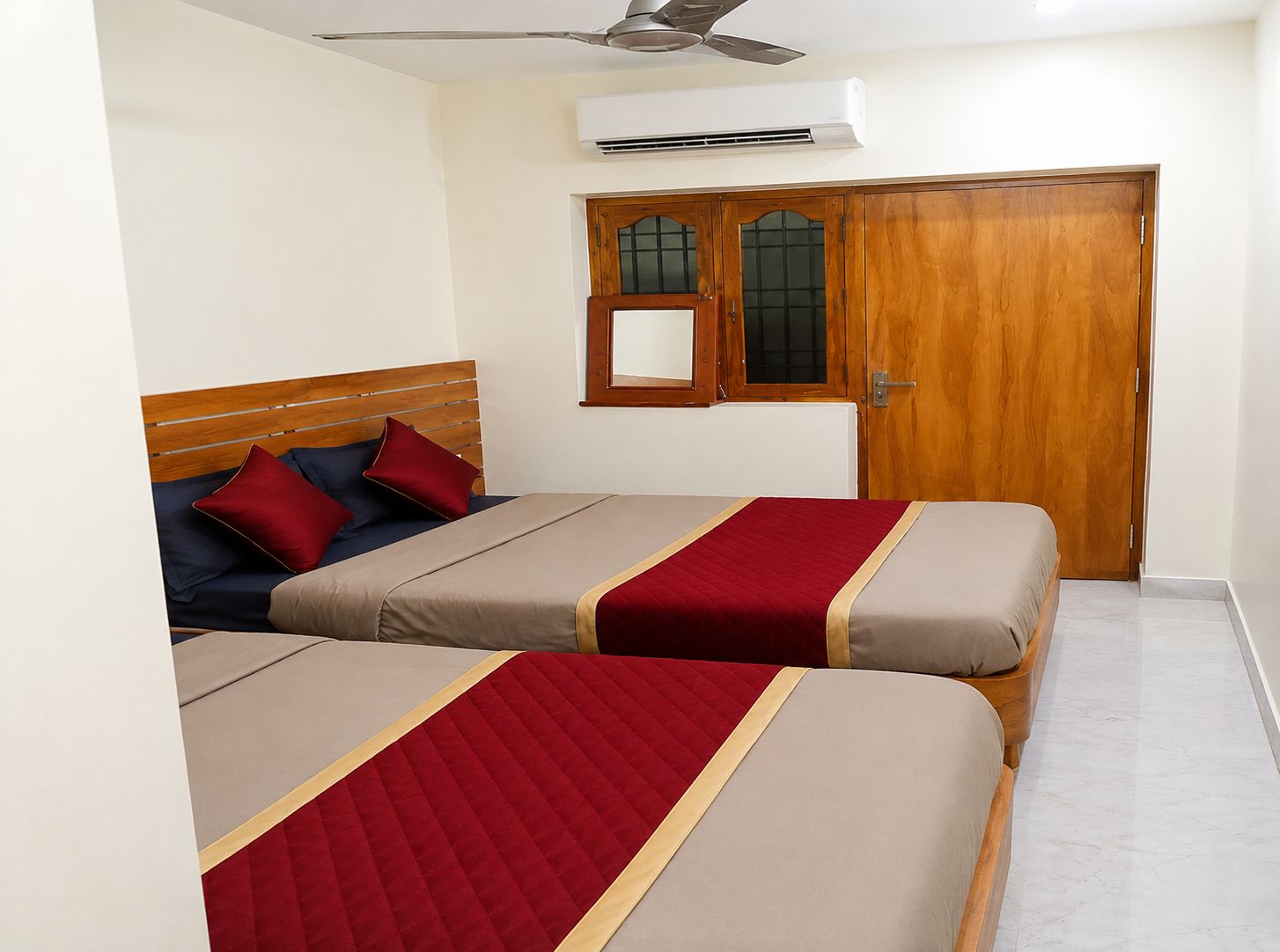 A bedroom with two beds, a wooden wardrobe, an air conditioning unit, and a window with a wooden frame.