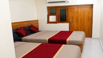 A bedroom with two beds, a wooden wardrobe, an air conditioning unit, and a window with a wooden frame.