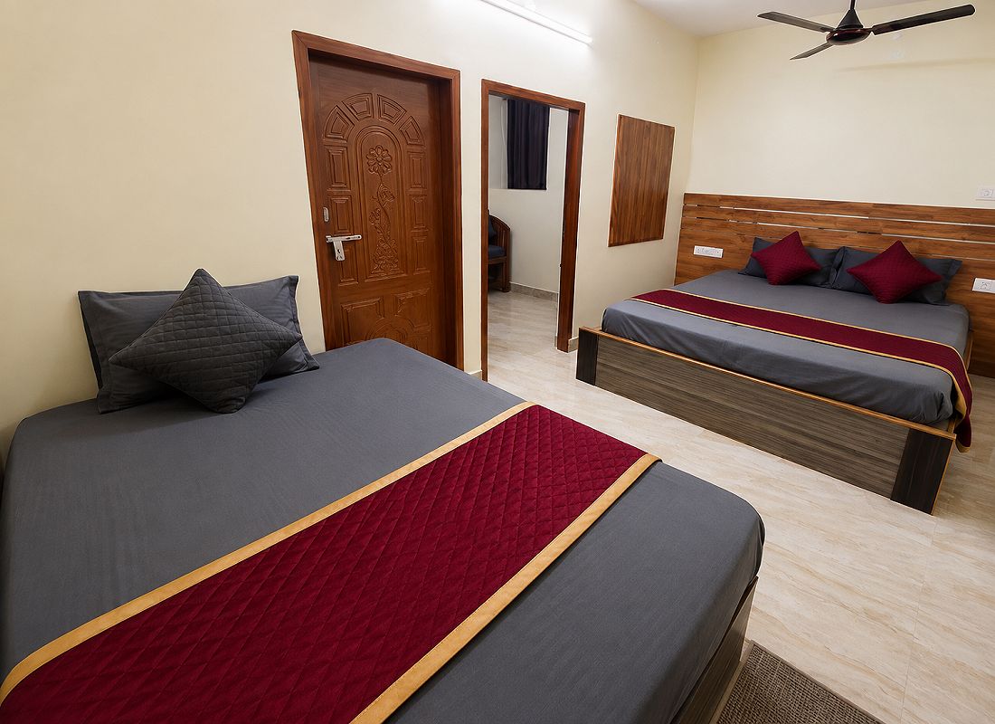A hotel room with two beds, a wooden door, a ceiling fan, and a view into the hallway.