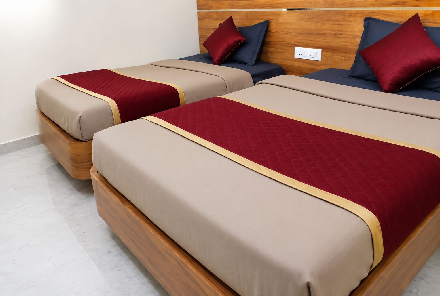 Two beds with wooden headboards, beige and red bedding, and dark pillows.