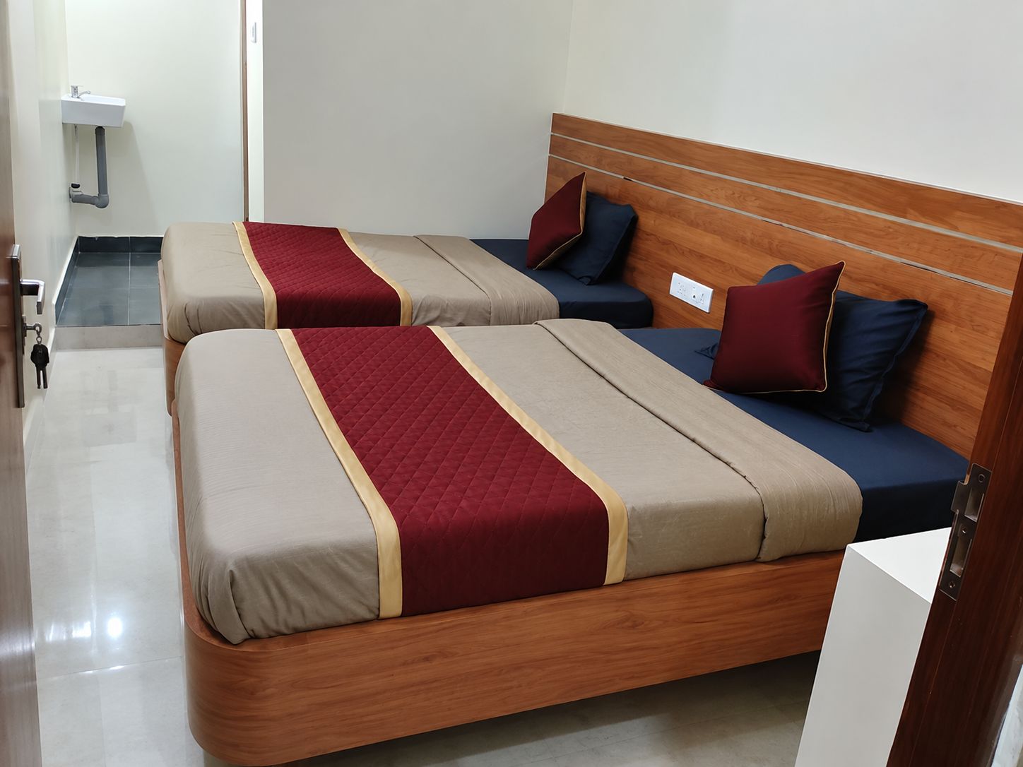 A hotel room with two beds, each with a wooden headboard, and a small bedside table.