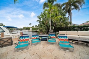 Eine Uferterrasse mit Liegestühlen, einer Couch und einem im Hintergrund liegenden Boot.