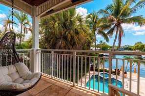 A balcony with a hanging chair, a pool, and palm trees. - Private Pool + Hot Tub + Boat Dock | 2-Min Walk to Beach | Beach Drive Estate (Delray Beach)