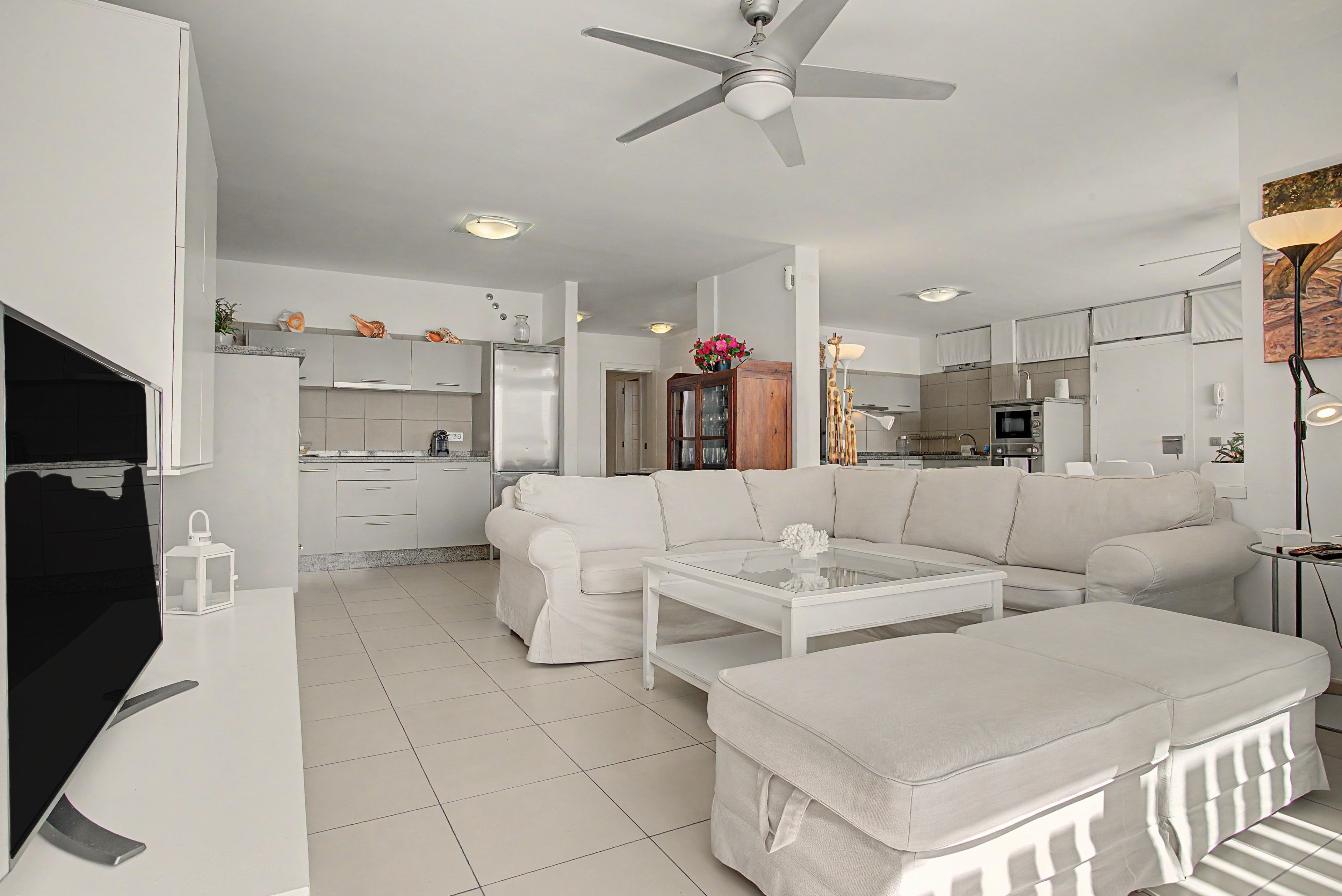 Una sala de estar moderna con un sofá blanco, una mesa de centro de vidrio y un ventilador de techo.