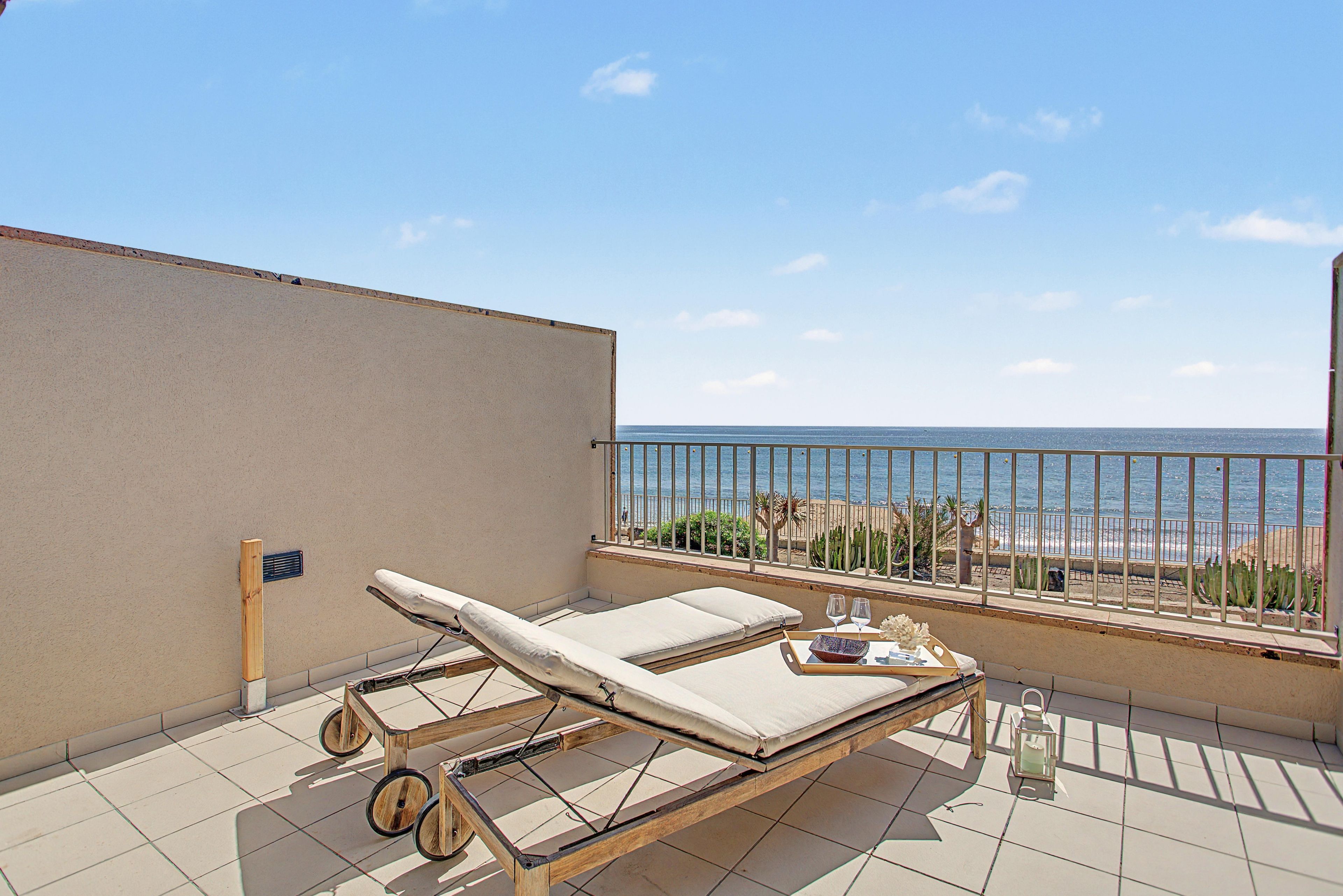 Un balcón con una silla de descanso, una mesita con bandeja y vista al mar.