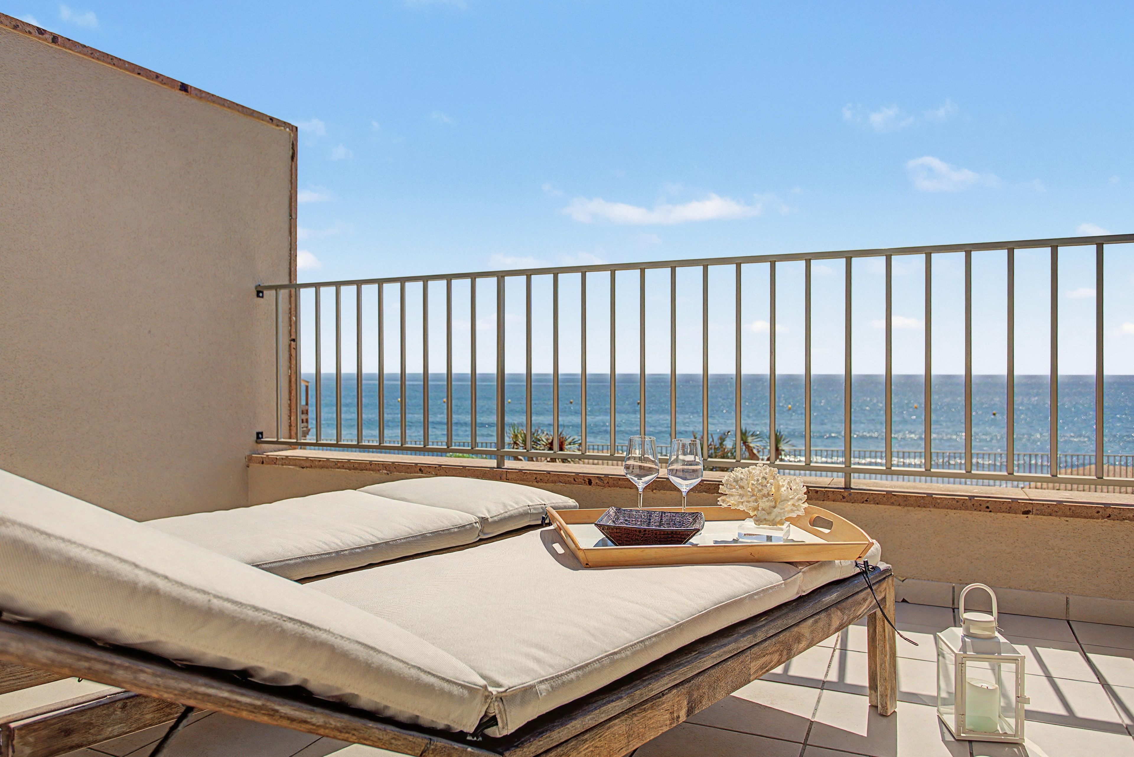 Ein Balkon mit Meerblick, eine Liege, ein Tablett mit Gläsern und ein Laternen.