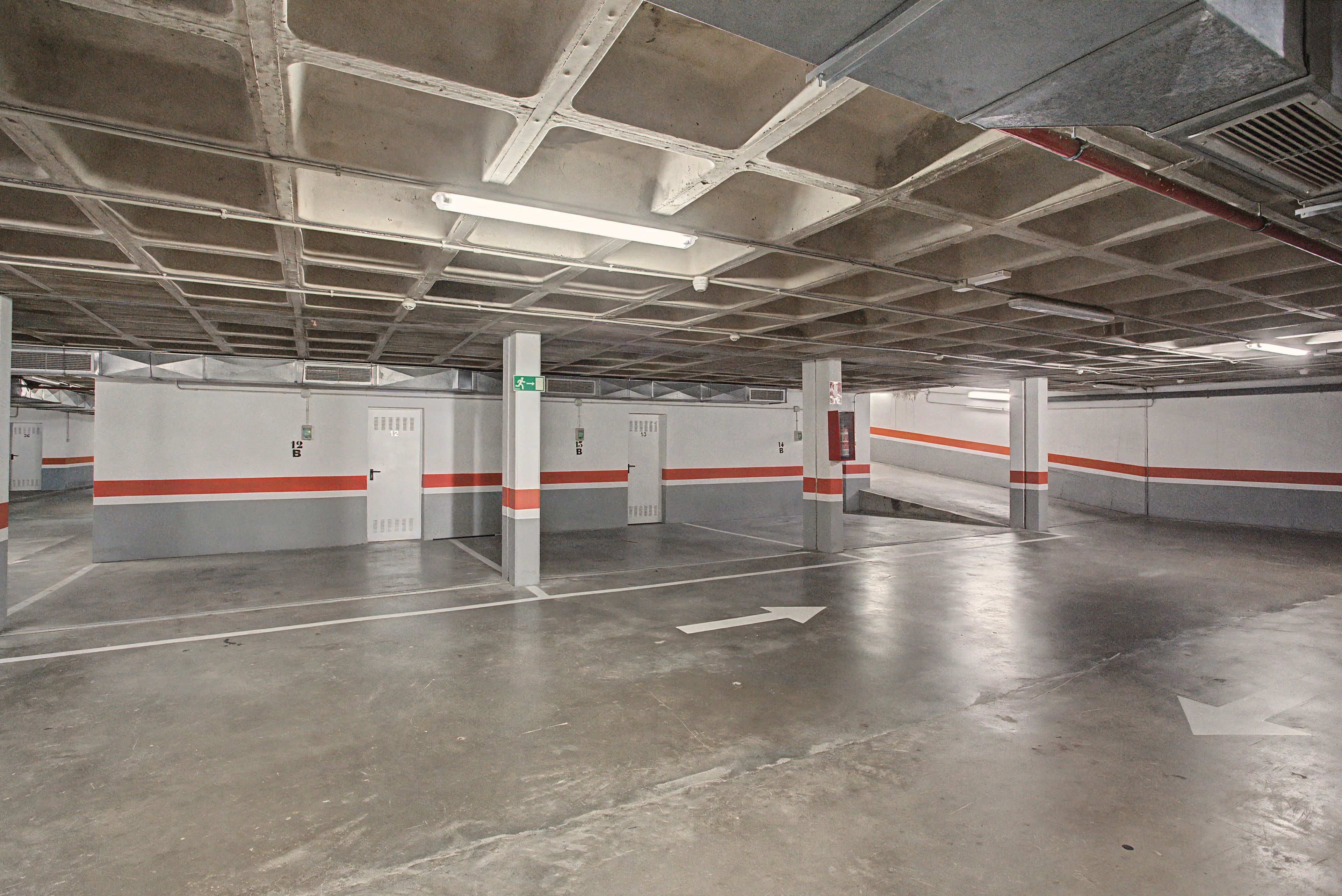 Un parking avec des piliers en béton, des flèches directionnelles peintes sur le sol et des panneaux indiquant les sorties de secours.