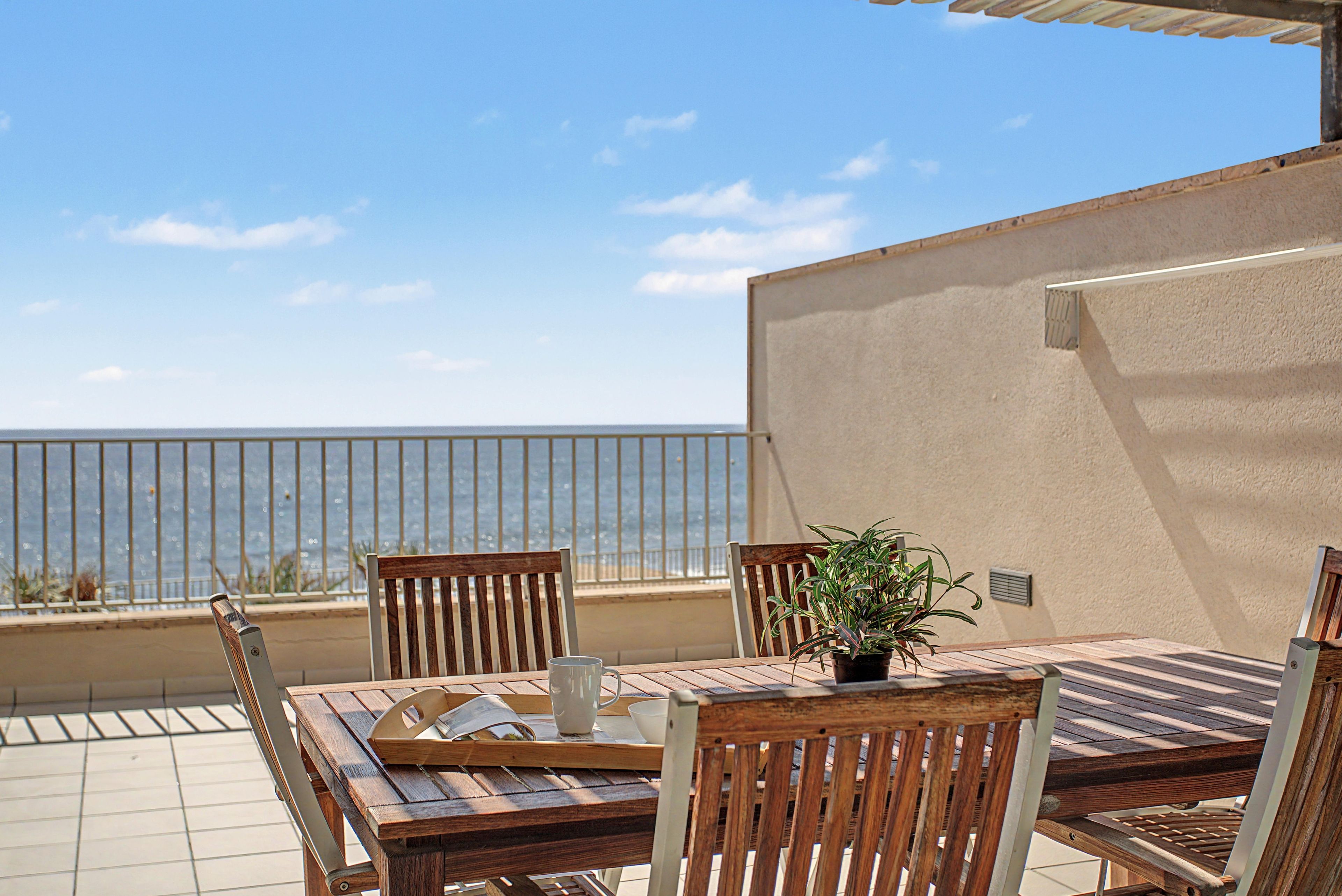 Eine Außenpatio mit Holztisch und -stühlen, einem Topfpflanzen und Blick auf das Meer.