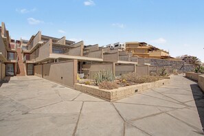 A residential building with multiple balconies, a courtyard with cacti, and a clear sky.
