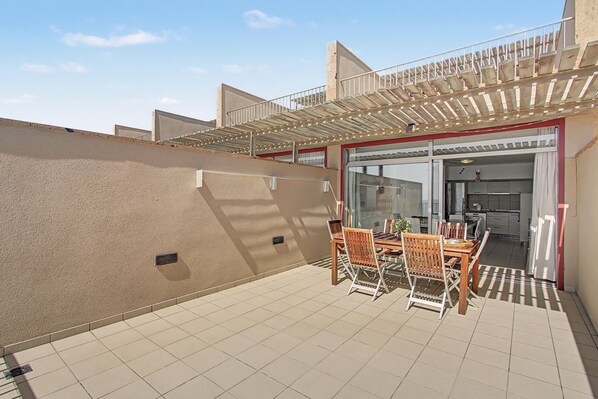 A patio with a table and chairs, a glass door leading to a kitchen, and a pergola structure.