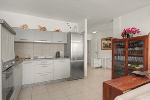 A modern kitchen with white cabinets, a stainless steel refrigerator, and a dining area with a wooden cabinet displaying glassware.