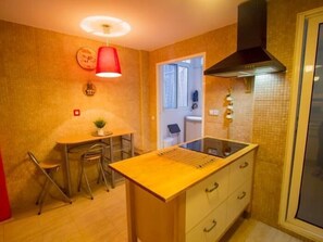 A compact kitchen with a dining area, a red pendant light, and a black range hood. - Sunstay Flat Torresol (Torremolinos)