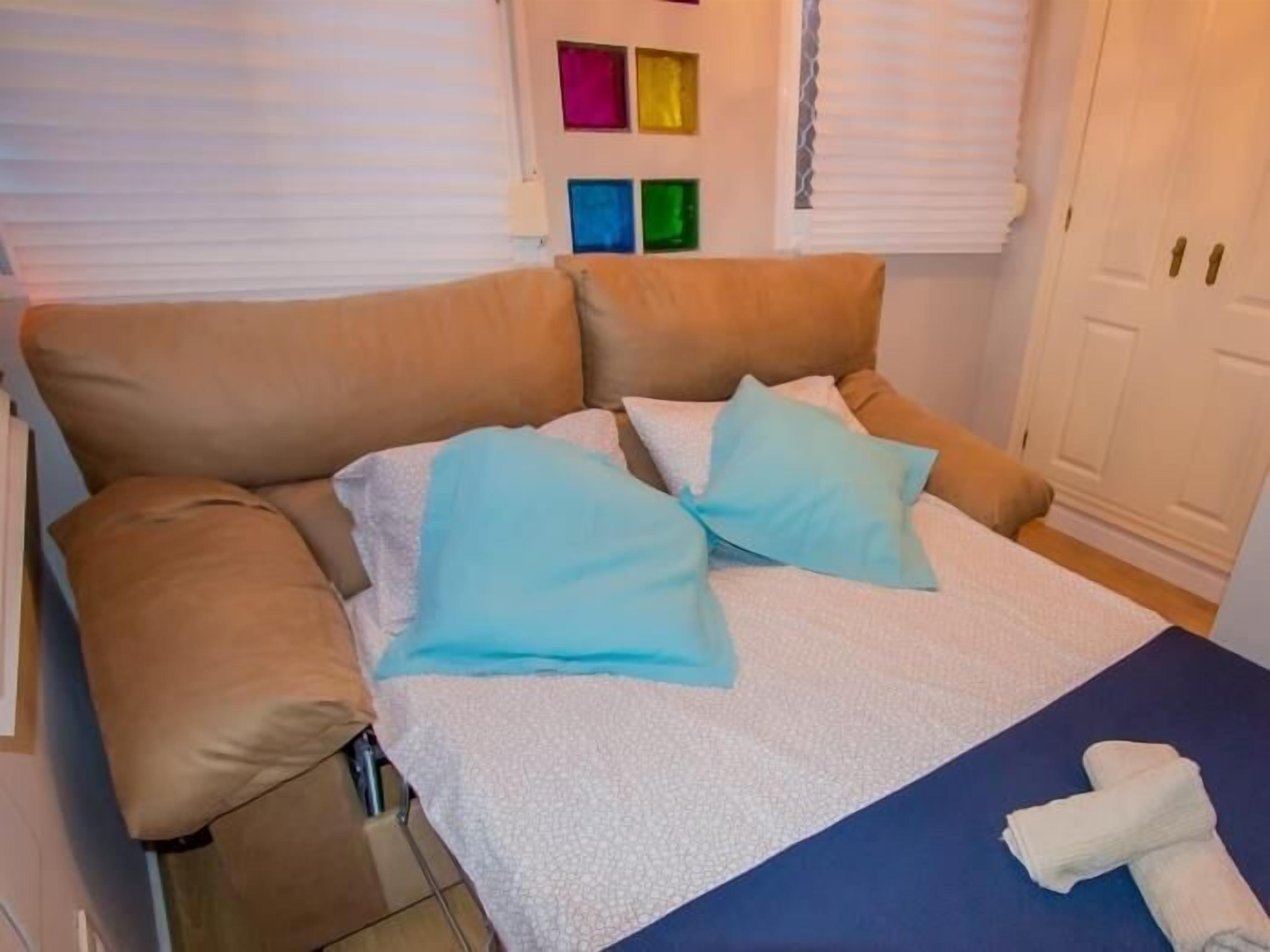 A bed with a white and blue bedspread, a beige sofa, and a blue towel on a blue table.