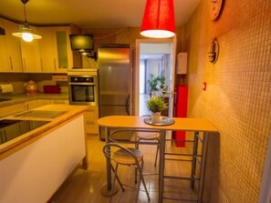 A compact kitchen with a central island, a dining area with two chairs, and a red pendant light. - Sunstay Flat Torresol (Torremolinos)
