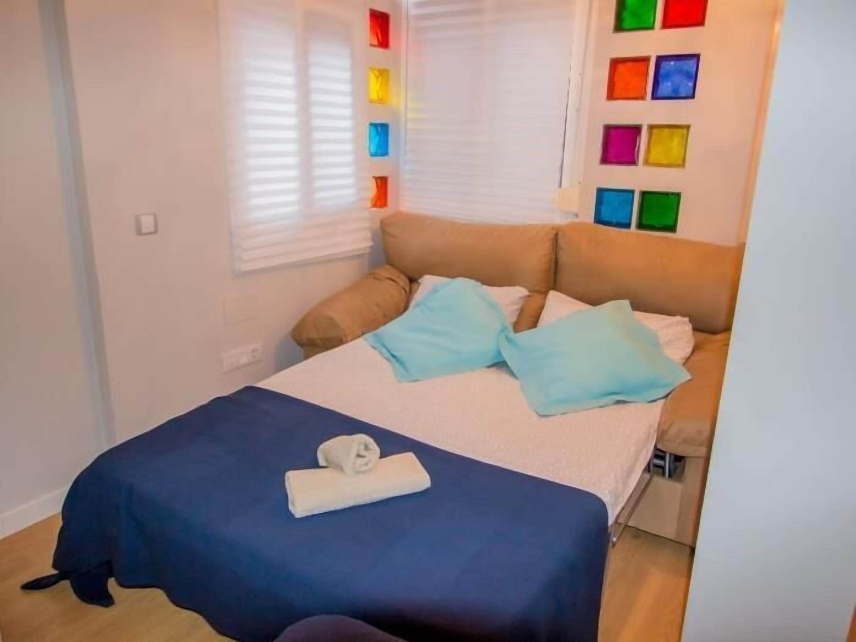 Un lit avec une couverture bleue, deux oreillers et une serviette enroulée.