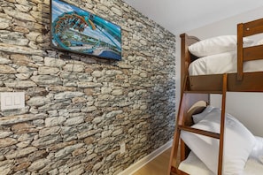 A room with a stone wall, a bunk bed, and a painting of a bridge. - Screened Pool + Hot Tub + Game Room | Gated Resort Near Parks | Palm & Play (Kissimmee)