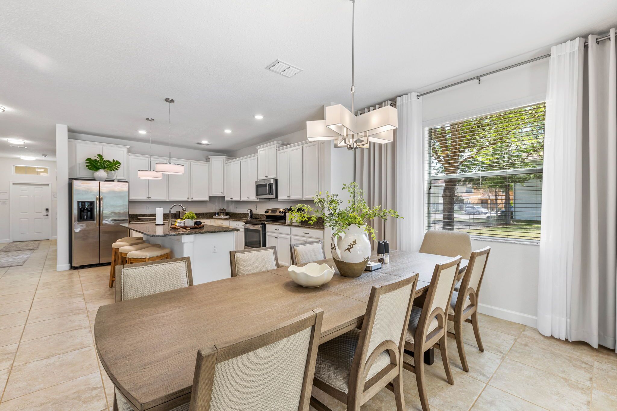 A modern kitchen with white cabinets, a central island, and a dining area with a wooden table and chairs.