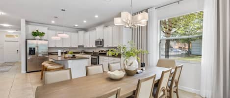 A modern kitchen with white cabinets, a central island, and a dining area with a wooden table and chairs.
