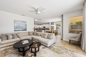 A modern living room with a sectional sofa, a coffee table, and a dining area in the background. - Screened Pool + Hot Tub + Game Room | Gated Resort Near Parks | Palm & Play (Kissimmee)
