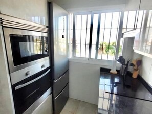 A kitchen with a built-in oven, a window with bars, and a countertop with kitchen utensils. - Sunstay Flat Centauro Mijas (Mijas)